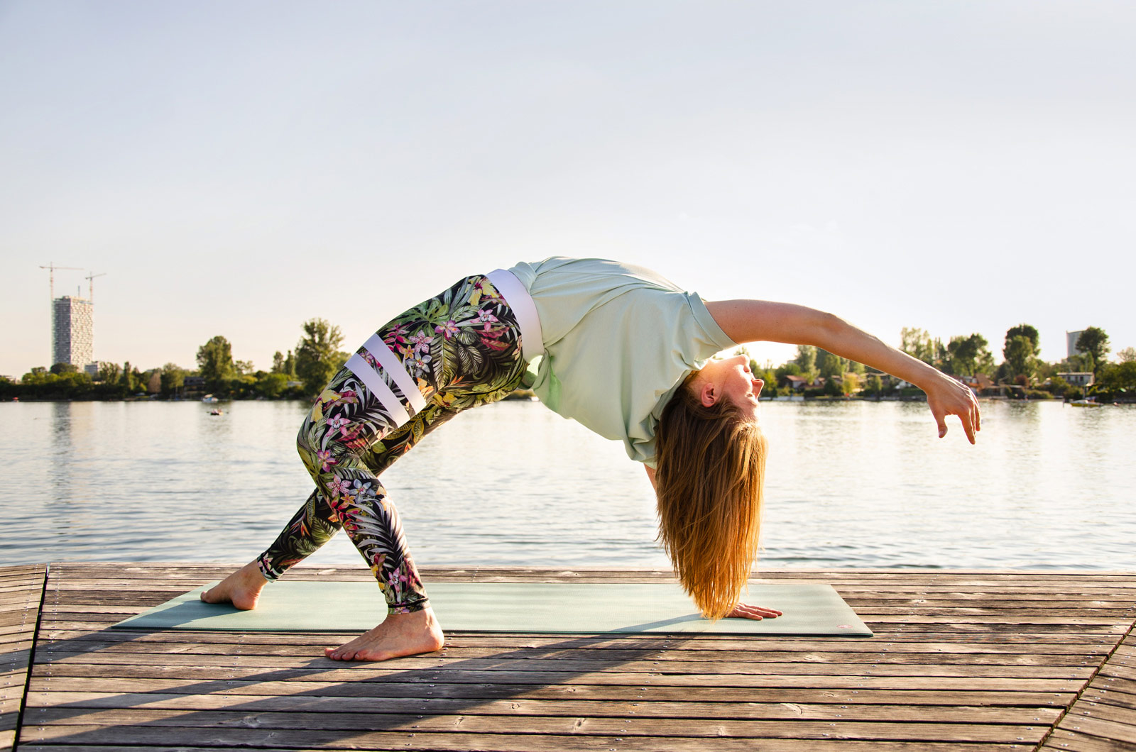 Die Yogalehrerin macht ihre Yogaübungen mit Yogamatte auf dem Holzsteg neben der alten Donau