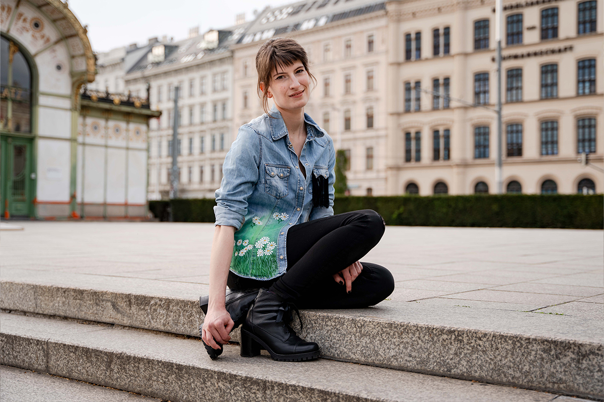 Silvia sitzt auf Stufen mit bemalter Jeansjacke, im Hintergrund Otto Wagner Architektur