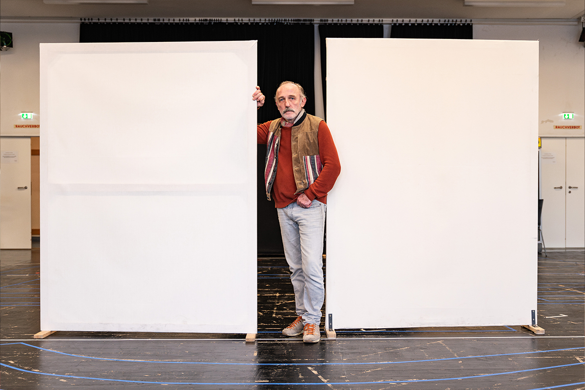 Der Schauspieler Karl Marcovics steht zwischen zwei aufgestellten weißen Leinwänden